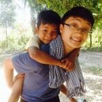 Shane Xiong, Singha Village, Cambodia with a child on his back