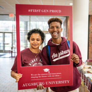Two students holding up a sign that says "First Generation Student"