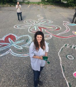 Greta McLain stands in a parking lot among large drawings of flowers on the concrete
