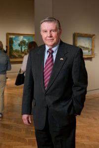 Joe (Orville C.) Hogander Jr. wears a suit and stands in an art gallery