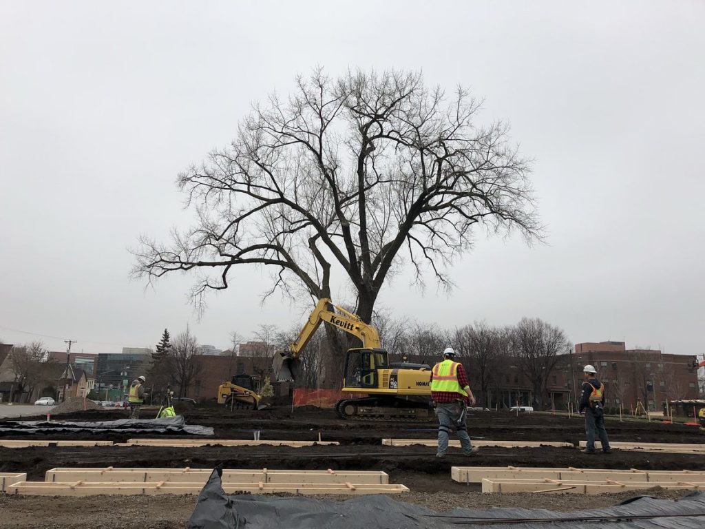 Construction crew members walk around low, rectangular wooden forms in the community garden area 