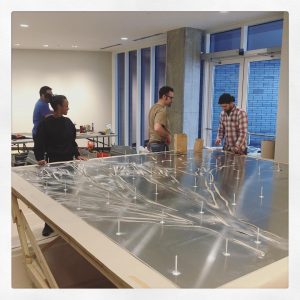 Four people work to ready a large art piece, resting on a table, for wall installation