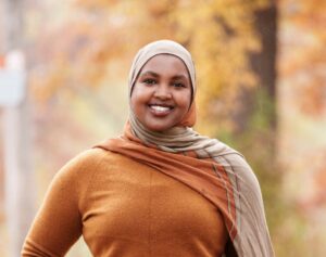 Nasrieen Habib poses in a tan hijab and orange dress