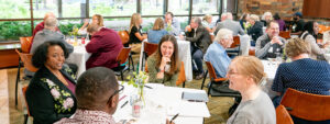 A meeting room with people sitting around multiple squared tables
