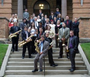 A group of people posing on the steps of Old Main, some holding musical instruments.