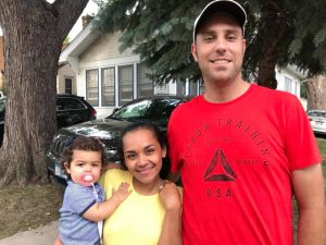 A family posing outdoors with a large tree and a house in the background.