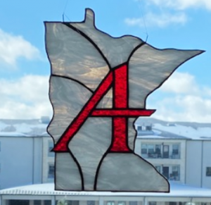 Stained glass ornament in the shape of Minnesota. The state is white and is overlayed with a red Augsburg 'A'