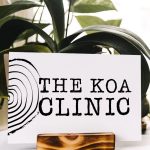 Sign that says "The Koa Clinic" in front of plant