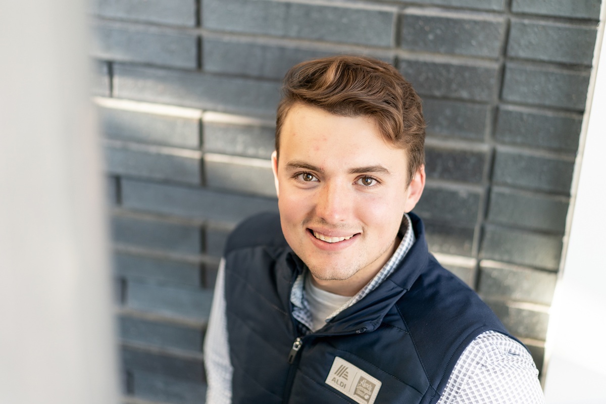 Max Milbrandt stands in front of a gray brick wall, looking up at the camera.