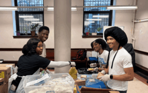 Students stand at a table, preparing food as a community service in New York, NY on Alternative Spring Break.