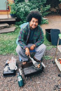 Tre smiling and tending a camp stove.