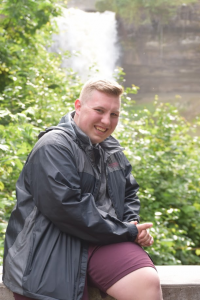 Ian smiling in front of a green background with waterfall in the distance