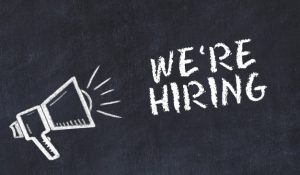clip art of megaphone announcing the words "we're hiring" with white font on dark background