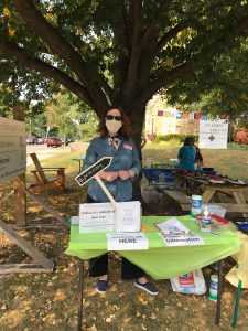 A member from Sts. Luke and James stranding out in their front porch at a table welcoming neighbors in the fall.