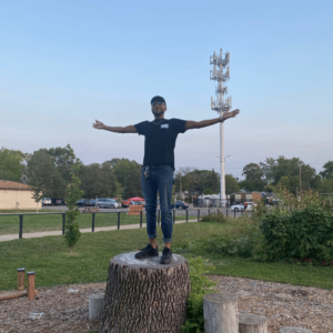 Geoffrey on top of a tree stump with his arms out to the side. 