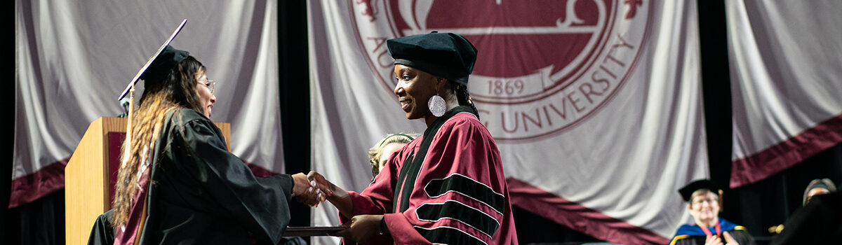 A student graduate shaking hands with a staff member while receiving diploma