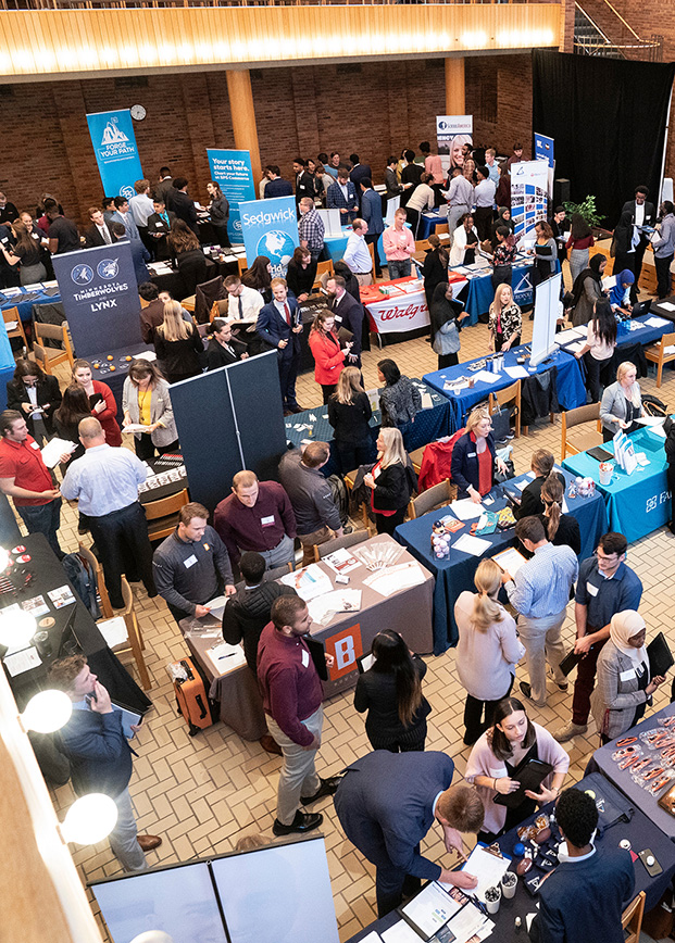 Aerial view of a busy career fair with multiple booths and attendees interacting.