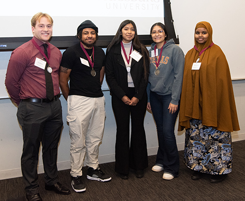 2024 Auggie Cup Five people standing in a row with medals around their necks in front of a screen.