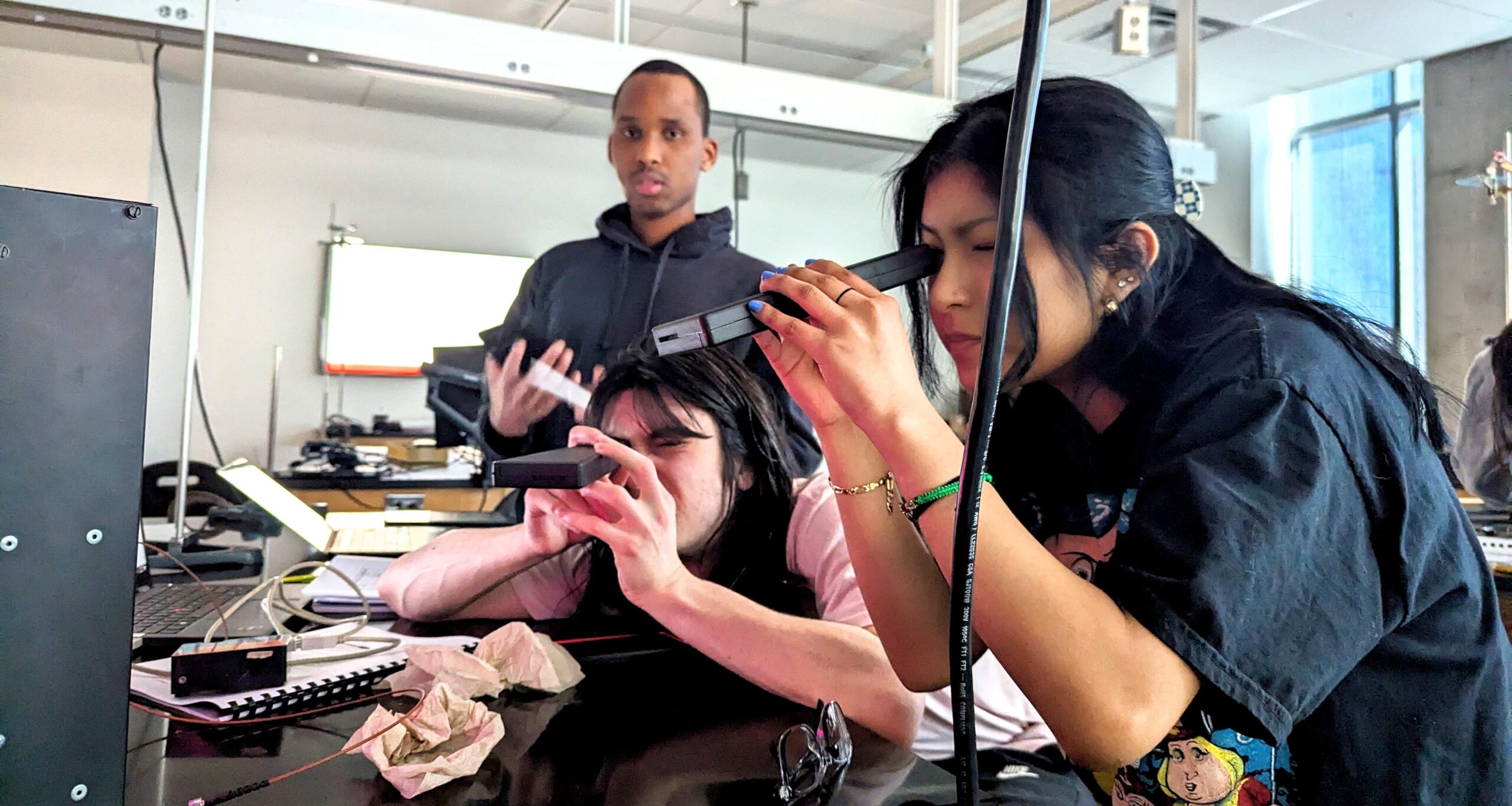 Students using handheld spectrometers observe gas discharge tubes.