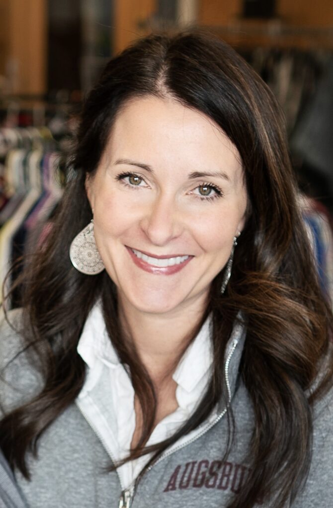 A smiling woman with dark brown hair, wearing a grey sweater with "Augsburg" embroidered in maroon.