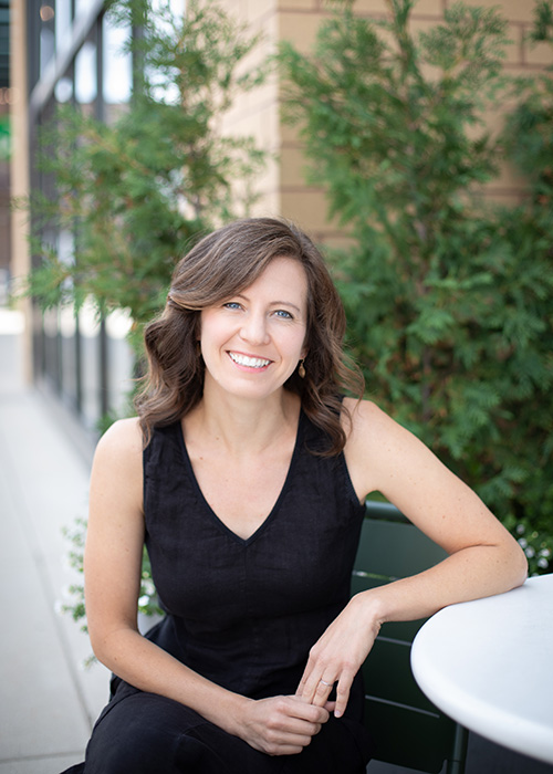A photo of Lindsay Starck: A woman wearing a black dress, smiling at the camera.