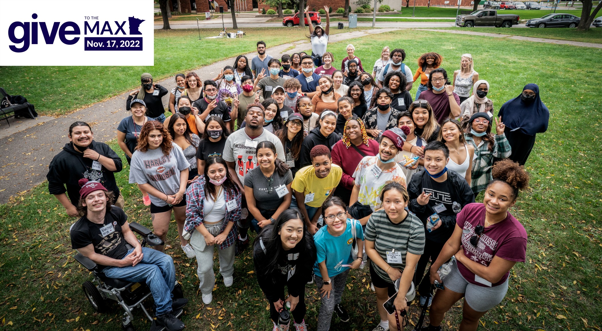 Large group of students gather to smile for a picture on Augsburg campus lawn.