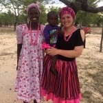 young women wear brightly colored dresses holding a young boy