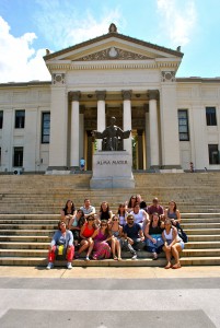 group of students sit on stone steps with large building with columns behind them