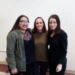 three women stand together in front of a white board