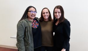 three women stand together in front of a white board