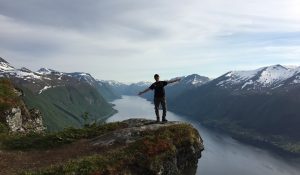 A person stands with arms outstretched with mountains in the background