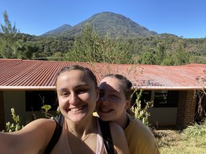 Two young women smile for a selfie in front of a mountainous background