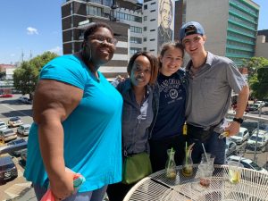 four people stand on a balcony with tall buildings in the background