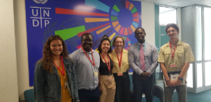 six people wearing lanyards stand in front of a UNDP mural