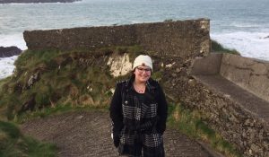 a young woman stands in front of crashing ocean waves in Ireland