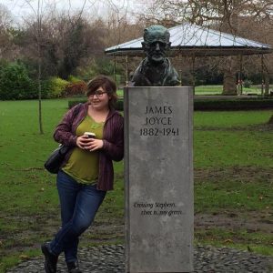 a young woman stands next to the gravestone of James Joyce