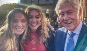 Two young woman shake hands with Bill Clinton