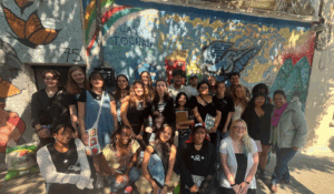 A group of over 20 college students pose in front of a colorful mural in Mexico City