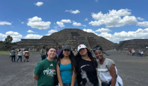 A group of four college students pose smiling in front of the Teotihuacan Pyramids