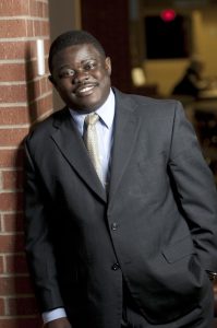 Black male in suit leaning against brick wall