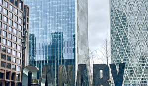View of Canary Wharf with reflective "CANARY WHARF" sign and modern skyscrapers.