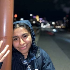 Woman in a blue hooded jacket leaning against a post