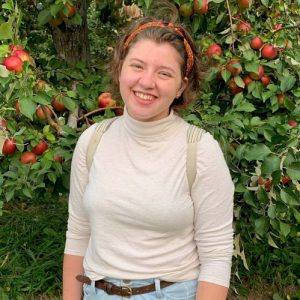 Woman in a white turtleneck in front of an apple tree