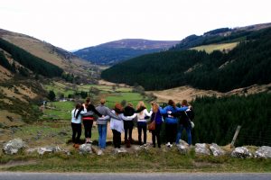 A group of nine students look out over a valley with their arms around each other and their backs to the camera