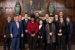 The 2023 Augsburg Innovation Scholars team, faculty mentors, and Augsburg leaders pose in front of a fireplace and wood-paneled walls at the Mayo Clinic in Rochester, MN.