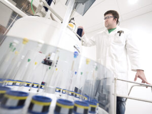 Michael Wentzel is wearing a white lab coat and green t-shirt and working on a chemistry experiment in a lab.