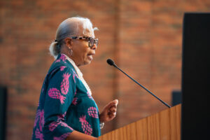 Dr. Gloria Ladson-Billings wears a blue and pink dress and white necklace as she delivers a lecture in the chapel.