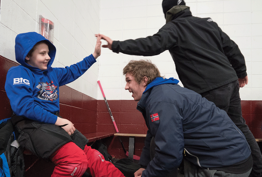 Kristian Evans ’19 helps a member of the DinoMights Squirt team prepare for hockey practice. Players are 10 or 11 years old.