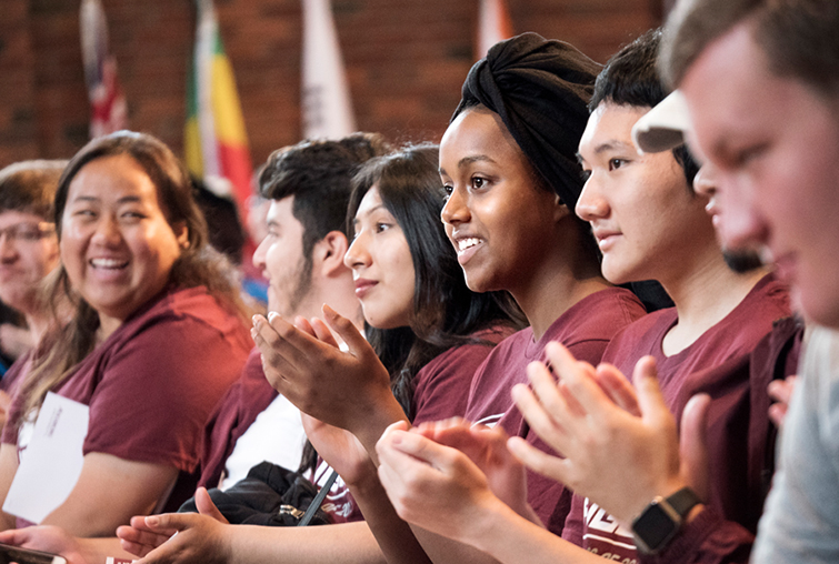 Seated students clapping and smiling at chapel