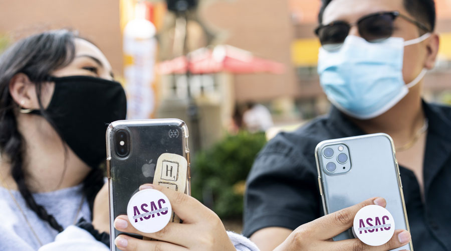 Two students with masks on holding their phones showing off their ASAC pop sockets